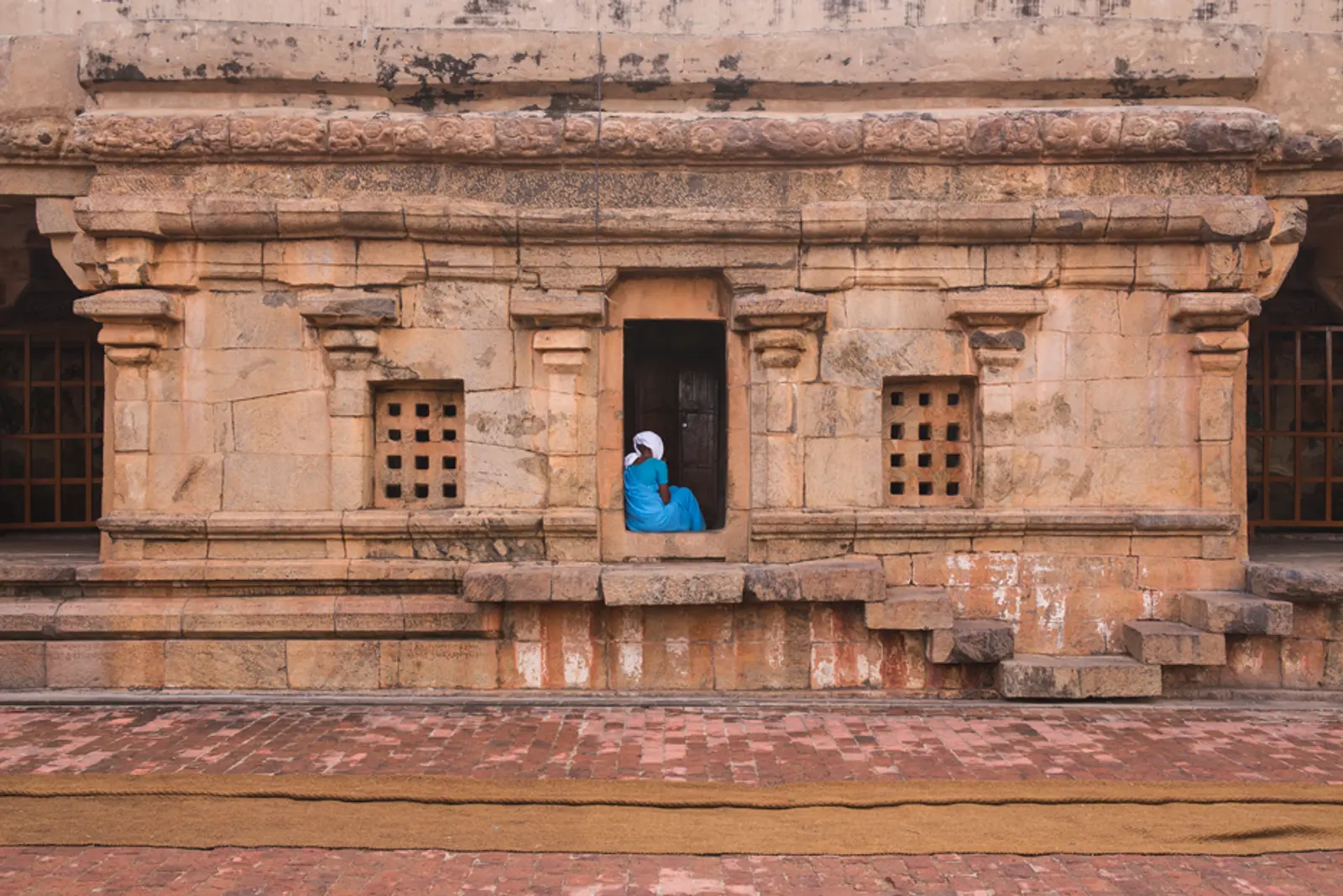 Someone in blue resting in a doorway of a carved stone temple wall in Thanjavur, Tamil Nadu